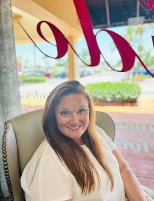 Sunlit woman with long red hair sitting in a cozy cafe in In The Shade, Florida, showcasing a relaxing atmosphere perfect for casual dining and coffee.