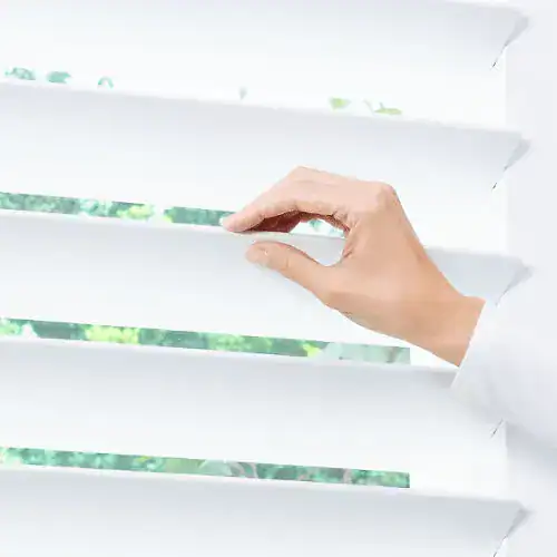 Close-up of a hand adjusting white window blinds, controlling natural light and privacy in home or office. Modern window treatment for sunlight control and aesthetic appeal.