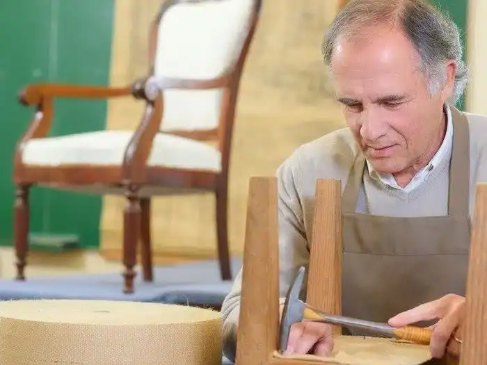 Detailed image of an elderly man carefully shaping wood with a chisel, demonstrating craft skills in woodworking.