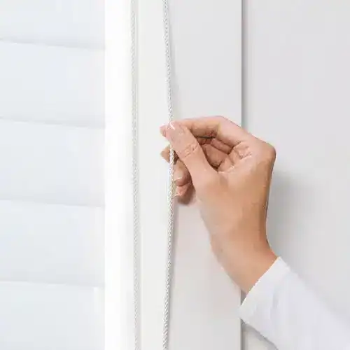 Close-up of hand adjusting vertical blinds cord in modern home interior.