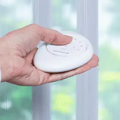 Hand holding panic button near window, home security device for emergencies, safety alarm, emergency response button, portable security alert system.