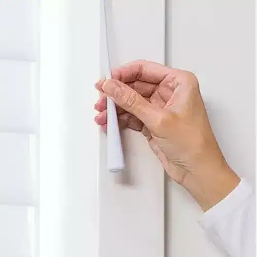 Close-up of a hand peeling off wallpaper from a white wall, showing home improvement and wall renovation process.