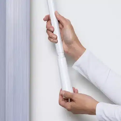 A person installing a white smart home security sensor on a wall, demonstrating home security device setup.