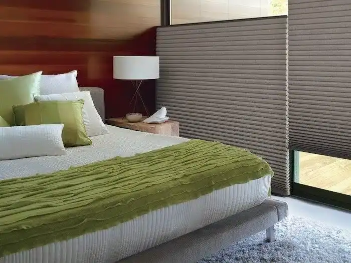 Comfortable bedroom with neutral decor, green bedding, and large window with blinds indoors.